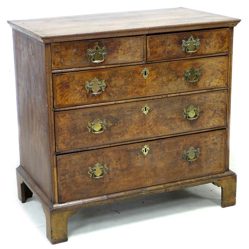 An early 18th century walnut veneered and crossbanded chest of two short over three long graduating drawers, with later brass plate swan neck handles and later shield shaped brass escutcheons, raised on bracket feet, 100 by 58.5 by 96 cm high.