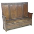 A 17th century oak box settle, with four panel back decoratively carved foliate and lunette frieze, ... 