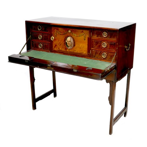 A fine and rare late 18th century Swedish Gustavian campaign desk by Georg Haupt, master in Stockholm 1770-1784, the mahogany chest form body with line inlaid detail and twin gilt brass hinged carry handles to the sides, an oval escutcheon to the front fold down section, opening to reveal a fitted interior with six drawers flanking a central cupboard, inset with an oval painted oil on canvas portrait of a gentleman, framed by an inlaid and stained laurel wreath tied with ribbons against a satinwood veneered background, the fall front with integral lift slope and fold out section with three carved recesses, all raised on two pairs of folding square section legs and a fold out front apron, with brass stays and sprung retaining lock, signed into the inlay of the lower corners of the central portrait panel 'G. Haupt fecit a Stockholm', 105 by 49 by 47.5cm high, 105cm high with legs extended.