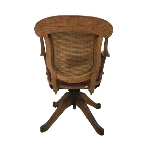 180 - An Edwardian oak office / desk swivel chair, with shaped arms, red leatherette seat and splat back, ... 