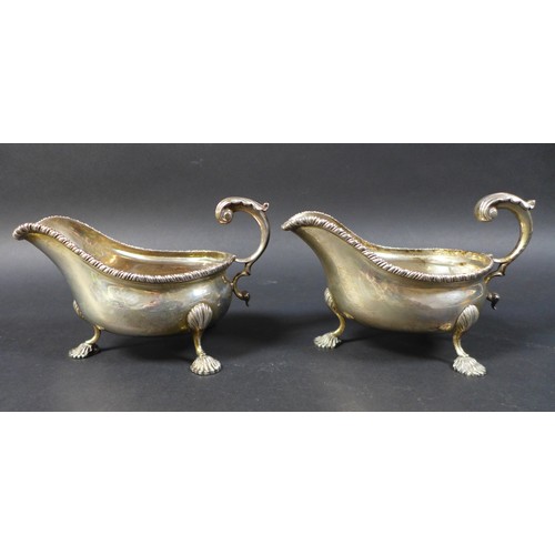 43 - A pair of Edwardian silver gravy boats, with a gadrooned rim and scroll handles, each raised on thre... 
