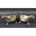 A pair of Edwardian silver gravy boats, with a gadrooned rim and scroll handles, each raised on thre... 