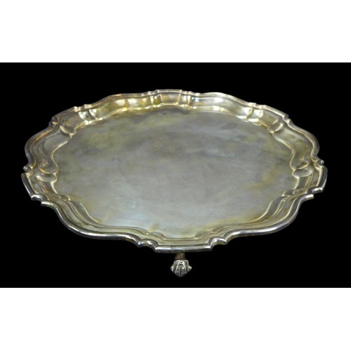 104 - A George V silver tray, of circular form with Chippendale pie crust edge, raised on three scroll fee... 