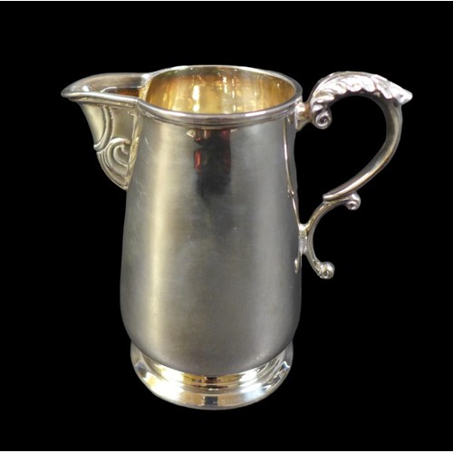 60 - An Irish silver milk jug, of tapering cylindrical form, with foliate thumb rest and double C scroll ... 