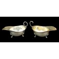 A pair of George V silver sauce boats, with reeded and foliate borders, raised upon tripod bases wit... 