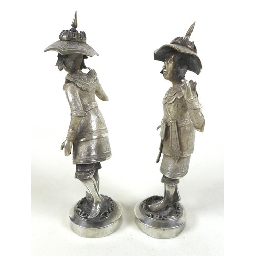 58 - A pair of Burmese silver figures, in traditional dress, holding large poles, raised on circular step... 