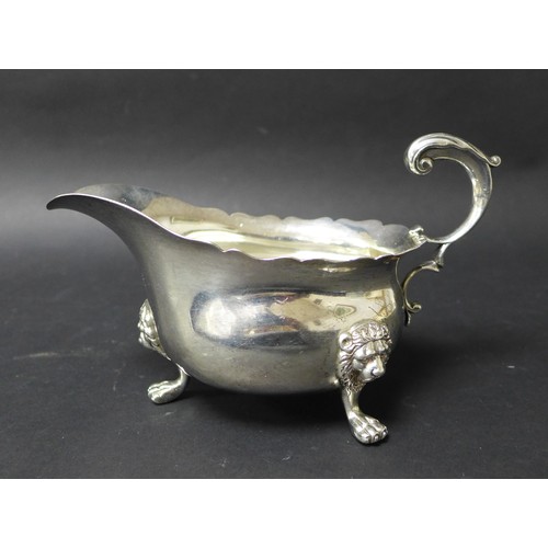 44 - An Victorian silver sauce boat, with scroll handle, scalloped top rim and raised upon three lion hea... 