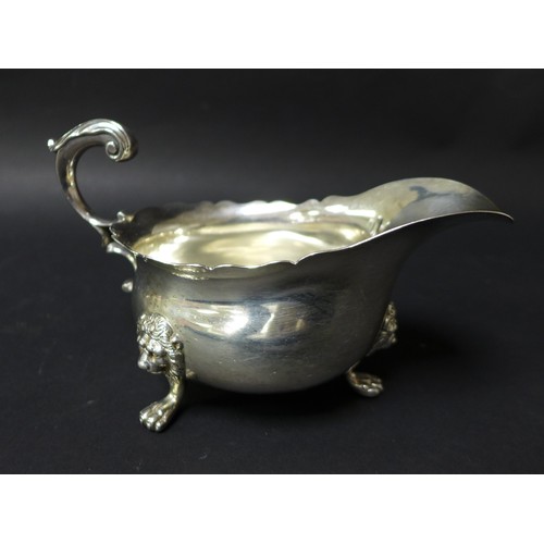 44 - An Victorian silver sauce boat, with scroll handle, scalloped top rim and raised upon three lion hea... 