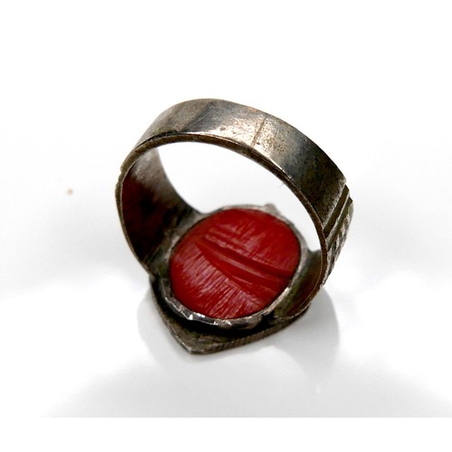 151 - A white metal ring, with carved and pierced crest and red coral backing, 21mm wide, size O/P, 5.9g.