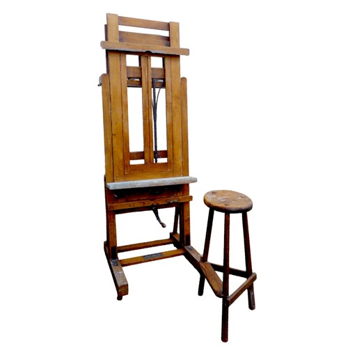 A large oak Windsor & Newton ‘Improved Studio Easel’, circa 1910, with metal fittings, dual action brass crank wheel, raised on four hardwood castors, one with screw brake, manufacturer's plaque to the base ‘Winsor & Newtons / Improved Studio Easel / Sold by All Artists Colourmen &c’, 74 by 71 by 201cm high, over 240cm high when fully raised, together with an Edwardian oak artist’s stool, circular seat raised on three hexagonal section legs joined by peripheral stretchers and foot rest to one side, inscribed to the underside of the seat, 44 by 36 by 78cm high. (2)
Provenance: this easel most recently belonged to the artist Barbara Balmer RSA RSW and the last work painted on it was purchased by the author J. K. Rowling!