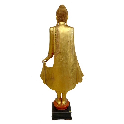 83 - A modern gilt carved wooden sculpture of a Burmese Mandalay Buddha, in standing position with arms o... 