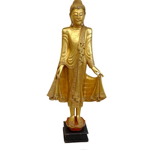 83 - A modern gilt carved wooden sculpture of a Burmese Mandalay Buddha, in standing position with arms o... 