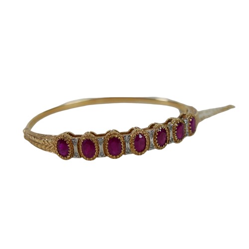 159 - A 9ct gold and ruby hinged bangle, set with seven oval cut rubies, in claw setting, interspersed by ... 