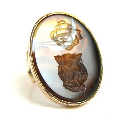 161 - A 9ct yellow gold signet ring, set with a large ornage, brown, and white hardstone carved with a mon... 