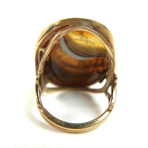 161 - A 9ct yellow gold signet ring, set with a large ornage, brown, and white hardstone carved with a mon... 