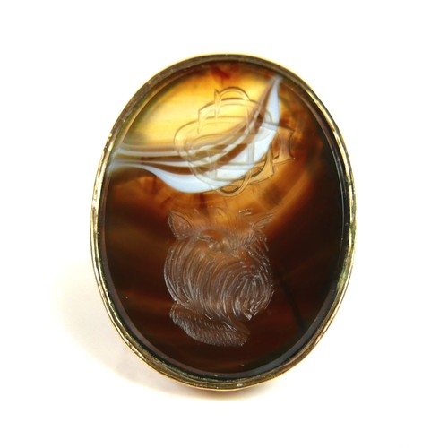 161 - A 9ct yellow gold signet ring, set with a large ornage, brown, and white hardstone carved with a mon... 