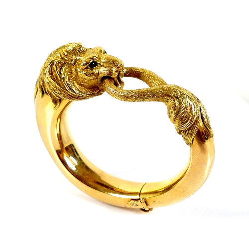 308 - An 18ct yellow gold hinged bangle, formed as a lion grasping it's tail in it's jaws, with inset cabo...
