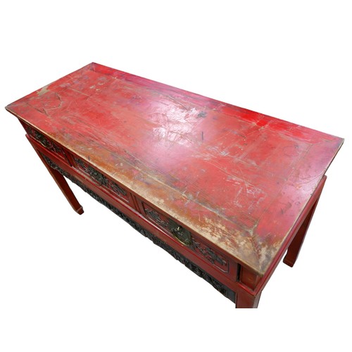 552 - A Chinese red lacquer three drawer hall table with a figural carved frieze, 138 by 56 by 88cm.