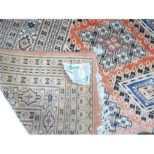 563 - A hand knotted woolen rug with a pink field and geometric design, 302 by 224cm.