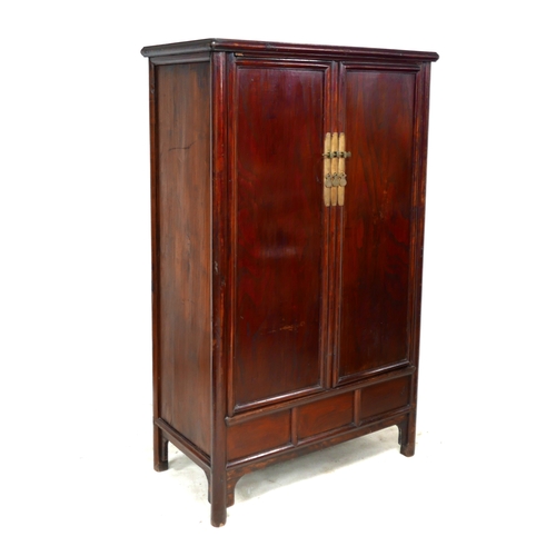 542 - A modern Chinese wooden cabinet, with brass lock, twin panelled doors enclosing shelves and two draw... 