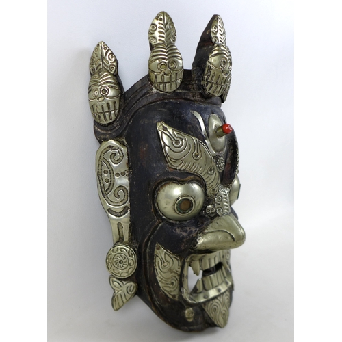 24 - A Nepalese carved wooden mask, white metal mounted, depicting the Wrathful Bhairava, 22 by 34 by 11c... 