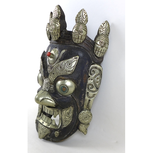 24 - A Nepalese carved wooden mask, white metal mounted, depicting the Wrathful Bhairava, 22 by 34 by 11c... 