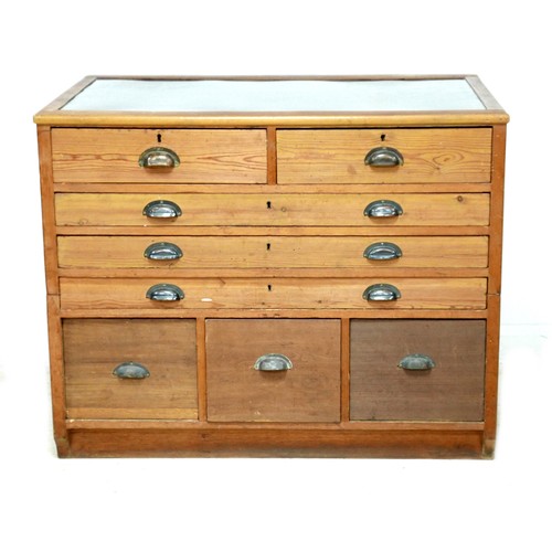 547 - A pitch pine plan chest, with inset black cloth surface, over an arrangement of eight drawers with b... 