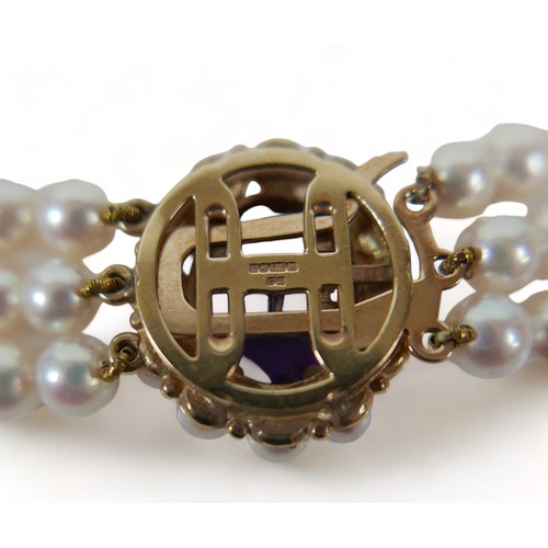 337 - A good quality triple string of pearls with a hallmarked amethyst set yellow gold clasp, 38cm long, ... 