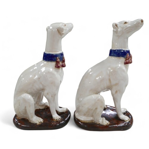 81 - A pair of pottery sculptures, modelled as white greyhounds, wearing blue collars with red tassels, o... 