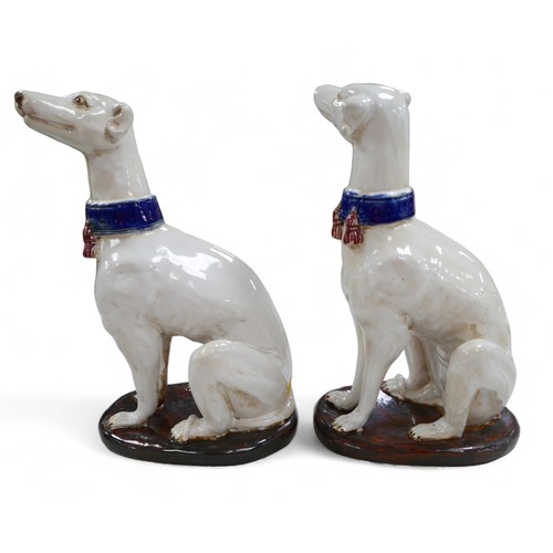 81 - A pair of pottery sculptures, modelled as white greyhounds, wearing blue collars with red tassels, o... 