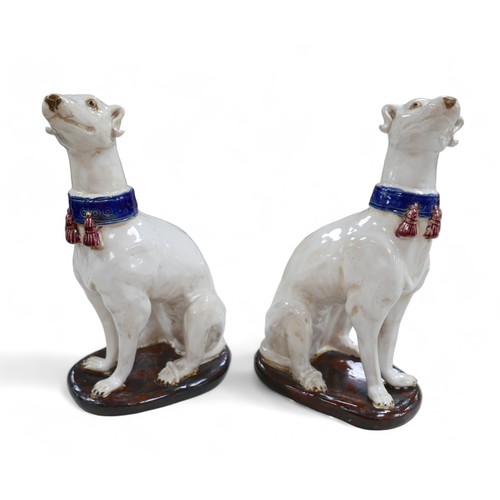 81 - A pair of pottery sculptures, modelled as white greyhounds, wearing blue collars with red tassels, o... 