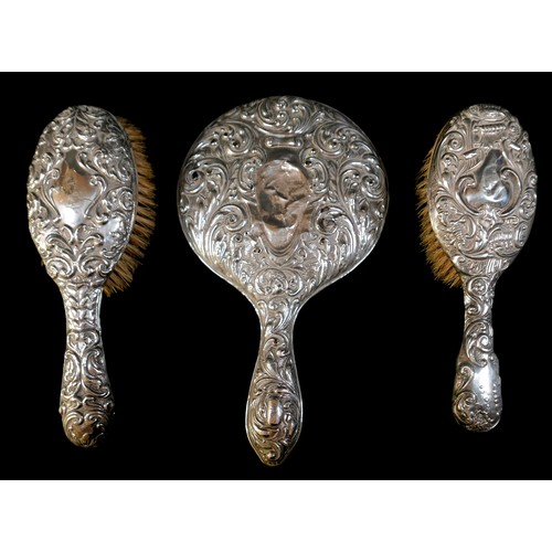 22 - A group of silver-backed dressing table items, comprising a hand mirror, two brushes with repousse d... 