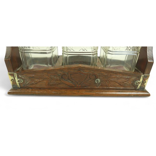 286 - A Victorian oak tantalus, with EPNS mounts and carved decoration, containing three clear glass part ... 