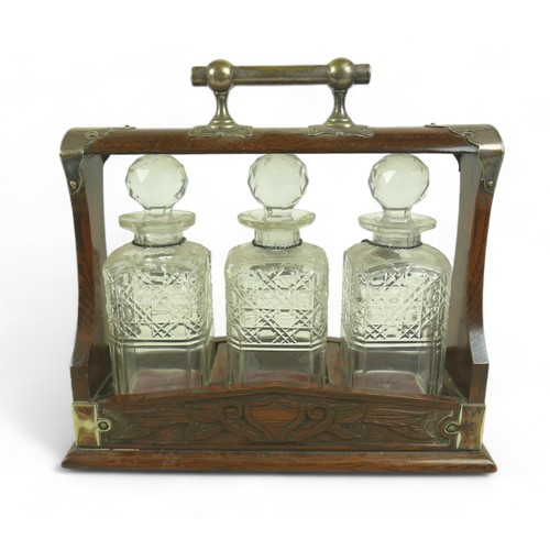 286 - A Victorian oak tantalus, with EPNS mounts and carved decoration, containing three clear glass part ... 