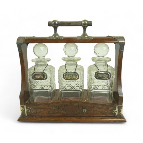 286 - A Victorian oak tantalus, with EPNS mounts and carved decoration, containing three clear glass part ... 