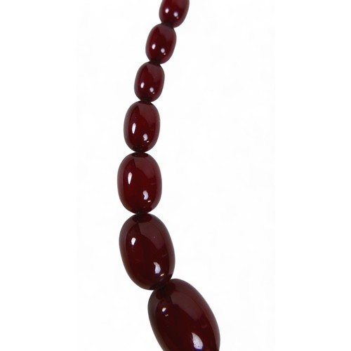 119 - A cherry amber bead necklace, of sixty graduating beads, largest bead 21.8 by 29mm, with screw clasp... 