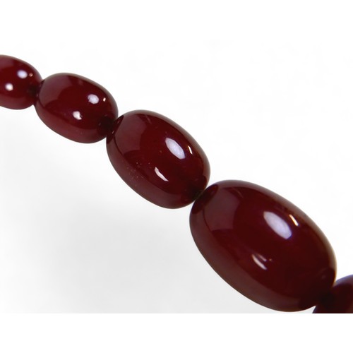 119 - A cherry amber bead necklace, of sixty graduating beads, largest bead 21.8 by 29mm, with screw clasp... 