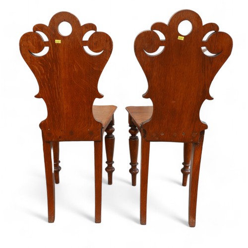 329 - A pair of Victorian oak hall chairs, on turned front legs, carved top rail and shield backs, ....