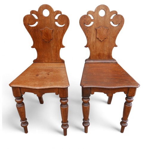 329 - A pair of Victorian oak hall chairs, on turned front legs, carved top rail and shield backs, ....