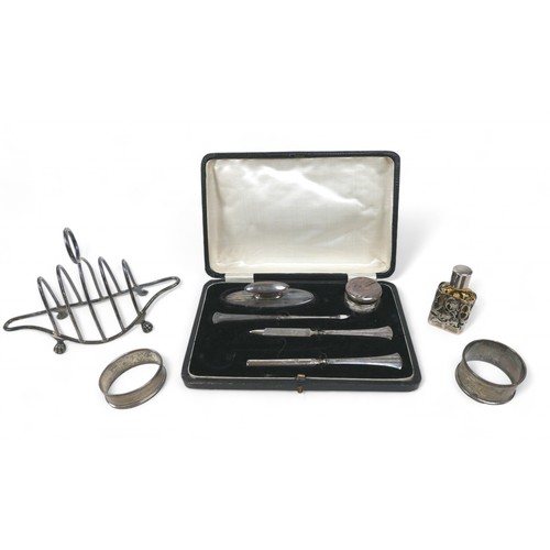 72 - A boxed part silver manicure set and four items of silver, comprising two napkin rings, a toast rack... 