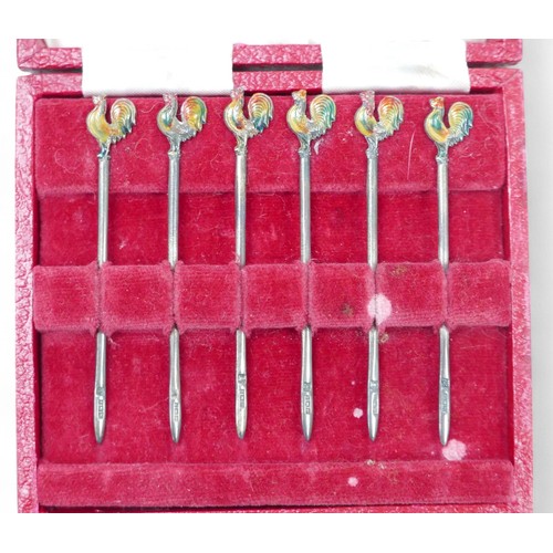 89 - A group of silver, comprising a cased set of six cocktail sticks with enamelled cockerel terminals, ... 