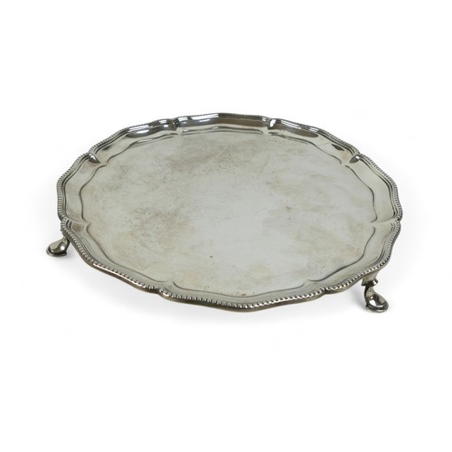 123 - A George V silver salver, with scalloped rim and beaded edging, raised on three hoof feet, Hawkswort... 