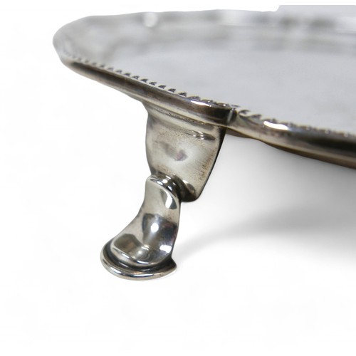 123 - A George V silver salver, with scalloped rim and beaded edging, raised on three hoof feet, Hawkswort... 