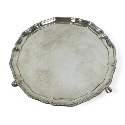 123 - A George V silver salver, with scalloped rim and beaded edging, raised on three hoof feet, Hawkswort... 