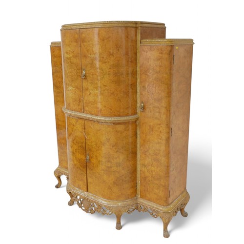 325 - A 20th century blonde burr walnut cocktail drinks cabinet, with two bow fronted doors enclosing a fi... 