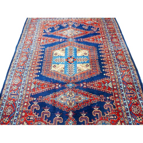 351 - A red ground hand knotted woollen rug, with geometric designs, 300 by 219cm.