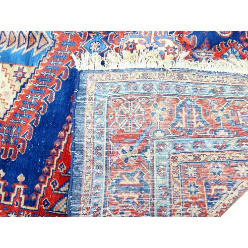 351 - A red ground hand knotted woollen rug, with geometric designs, 300 by 219cm.