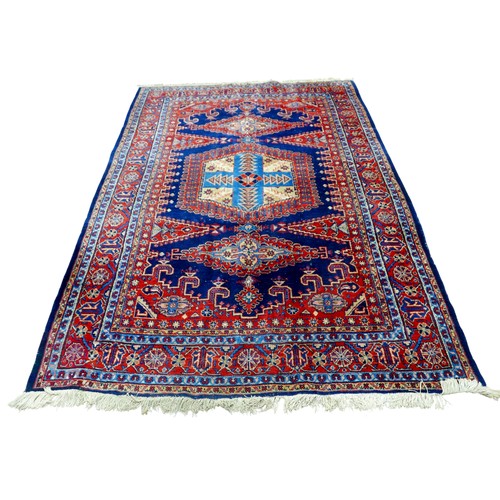351 - A red ground hand knotted woollen rug, with geometric designs, 300 by 219cm.