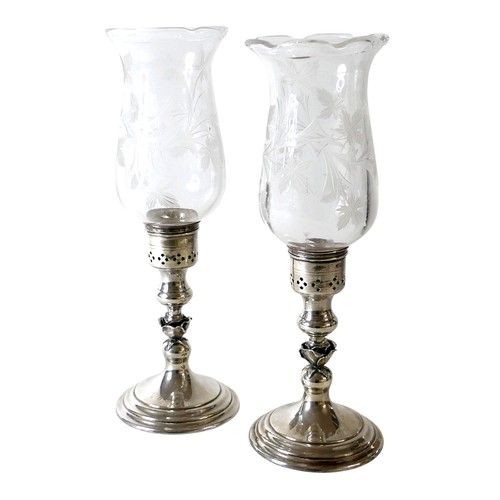 170 - A pair of Elizabeth II silver hurricane lamps with a rose column on a weighted circular footed base ... 