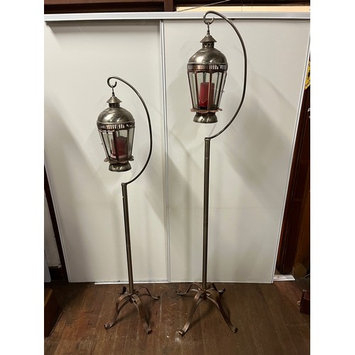 69 - Pair of graduated metal outdoor lantern stands with glass lanterns. Copper finish on curved foot sta... 